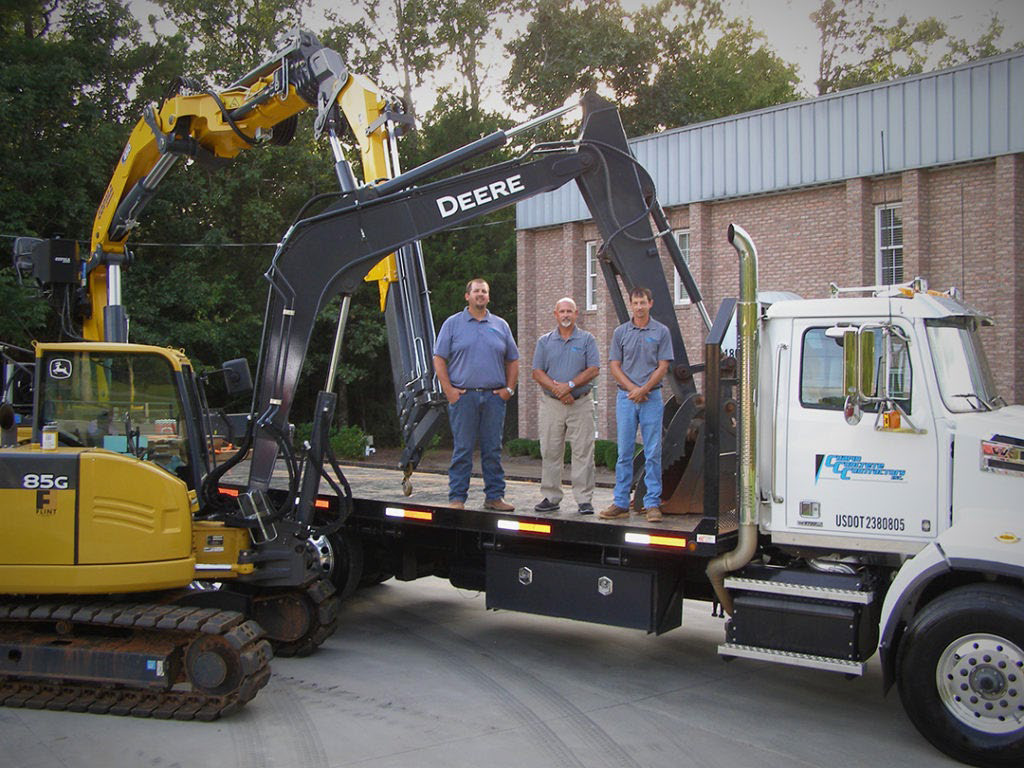 Three workers standing on a truck bed with construction equipment around.
