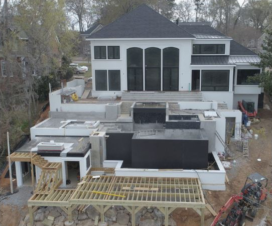 Modern multi-level house under construction with large windows and stone walls.